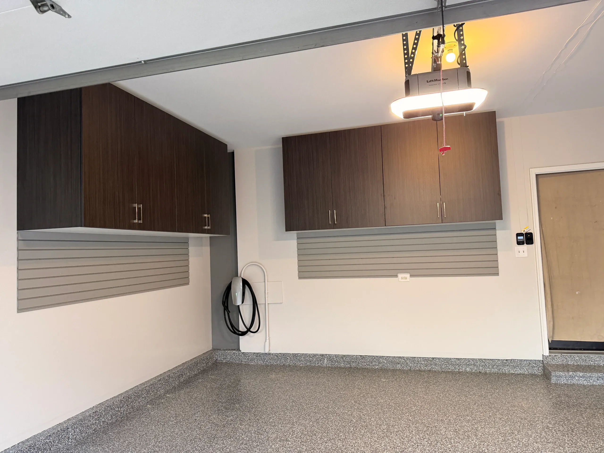 Close view of garage wall cabinets above grey slatwall with an EV charger mounted between runs