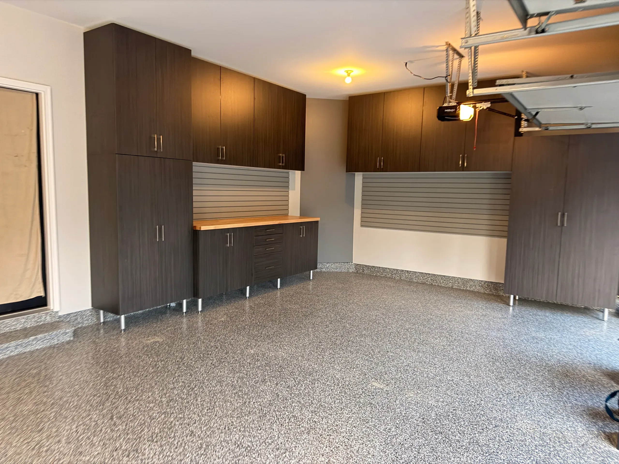 Finished garage with dark walnut wall cabinets, grey slatwall and a butcher-block workbench over a drawer bank